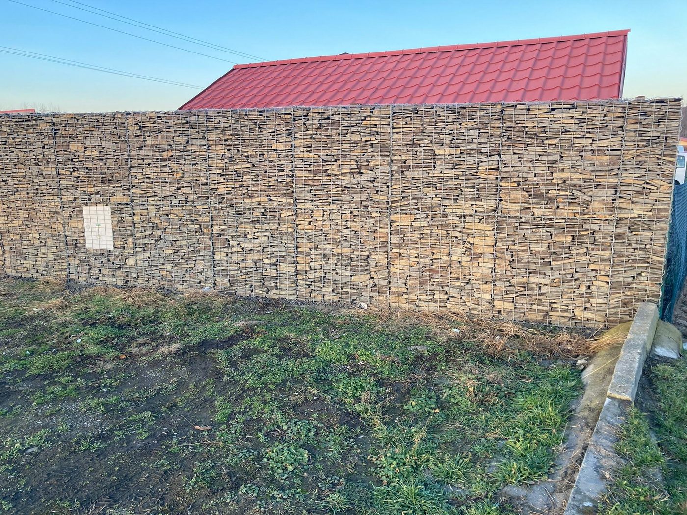 Gabionový múr pri dome s červenou strechou